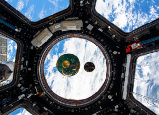 Das Bild zeigt das Missionsabzeichen Cosmic Kiss des ESA-Astronauten Matthias Maurer, das neben einer Nachbildung der Himmelsscheibe von Nebra in der Kuppel der Internationalen Raumstation mit sieben Fenstern schwebt.