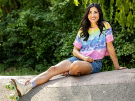 Junge Frau mit Rollschuhen sitzt auf einer Mauer.