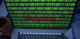 Laptopbiuldschirm mit binären Code (01110011010) und dem Wort Hackerangirff als Symbolbild für Cybercrime