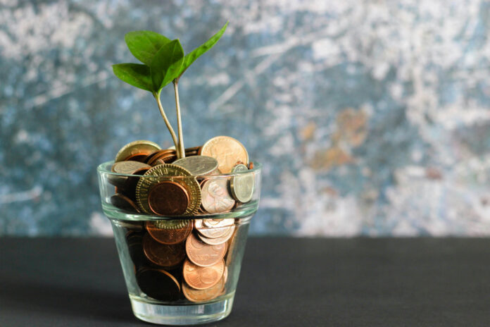 Symbolbild für Geldanlage, Ansparen, Sapren: Aus einem Glas mit Münzen wächst ein kleines Pflänzchen