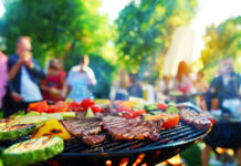 Fleisch und Gemüse auf dem Grill, im Hintergrund Menschen auf einer Gartenparty