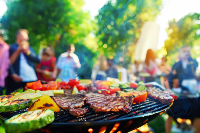 Fleisch und Gemüse auf dem Grill, im Hintergrund Menschen auf einer Gartenparty