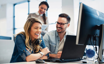Symbolbild Arbeitswelt, drei Menschen lachend vor einem Computer