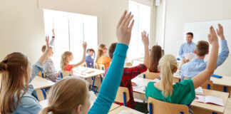 Symbolfoto für das Thema Finanzbildung, Schüler in einem Klassenraum, die aufzeigen