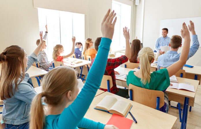 Symbolfoto für das Thema Finanzbildung, Schüler in einem Klassenraum, die aufzeigen