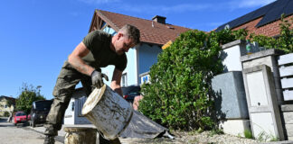 Soldat schüttet Schlammkübel aus als Symbolbild für die Aufräumarbeiten nach dem Hochwasser
