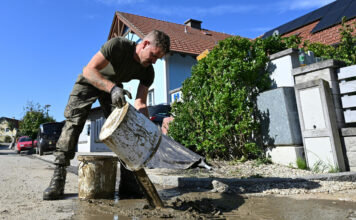 Soldat schüttet Schlammkübel aus als Symbolbild für die Aufräumarbeiten nach dem Hochwasser