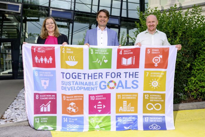 Petra Ibounig-Eixelsberger (Nachhaltigkeits­beauftragte), Gert Spanz und Wolfgang Saiwald (Projektmanager Nachhaltigkeit) hissen die SDG-Flagge.