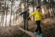 Vater und Sohn balancieren auf einem Baumstamm im Wald als Symbolbild für Unfallversicherung