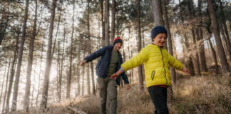 Vater und Sohn balancieren auf einem Baumstamm im Wald als Symbolbild für Unfallversicherung