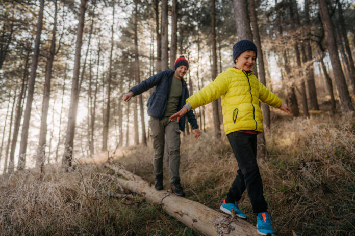 Vater und Sohn balancieren auf einem Baumstamm im Wald als Symbolbild für Unfallversicherung