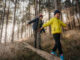 Vater und Sohn balancieren auf einem Baumstamm im Wald als Symbolbild für Unfallversicherung