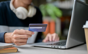 Sujetbild für Finanzbildung. Junger Mensch sitzt mit Kreditkarte vor einem Laptop.