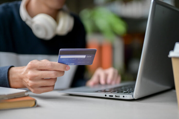 Sujetbild für Finanzbildung. Junger Mensch sitzt mit Kreditkarte vor einem Laptop.