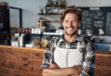 Cropped shot of a young shop owner looking happy while standing in his cafe