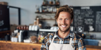 Cropped shot of a young shop owner looking happy while standing in his cafe