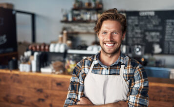 Cropped shot of a young shop owner looking happy while standing in his cafe