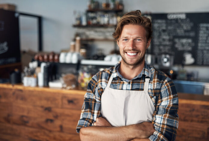 Cropped shot of a young shop owner looking happy while standing in his cafe