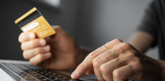 Symbolbild für sicheres Bezahlen im Internet, Person mit Kreditkarte in der Hand sitzt vor einem Laptop