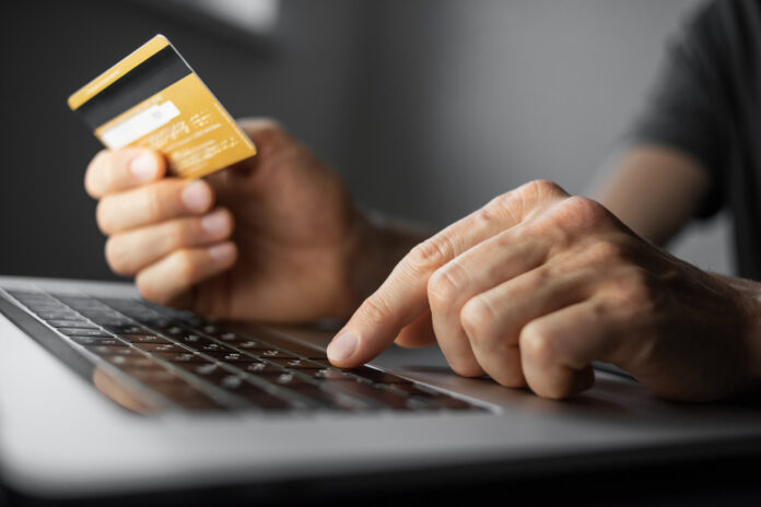 Symbolbild für sicheres Bezahlen im Internet, Person mit Kreditkarte in der Hand sitzt vor einem Laptop