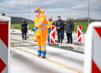 Ein Mann in Seuchenanzug spritzt auf den Seuchenteppich als Prävention gegen die Maul- und Klauenseuche. Im Hintergrund steht Landwirtschaftsminister Norbert Totschnig.