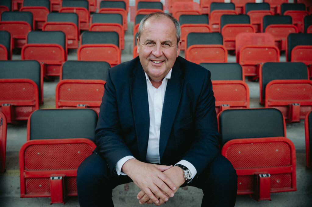 Josef Pröll sitzt in den Rängen eines Fußballstadions