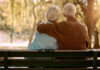 Love, hug and old couple in a park on a bench for a calm, peaceful or romantic summer marriage anniversary date. Nature, romance or back view of old woman and elderly partner in a relaxing embrace.