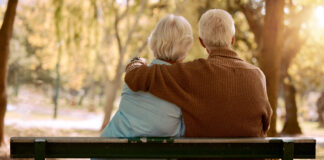 Love, hug and old couple in a park on a bench for a calm, peaceful or romantic summer marriage anniversary date. Nature, romance or back view of old woman and elderly partner in a relaxing embrace.