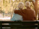 Love, hug and old couple in a park on a bench for a calm, peaceful or romantic summer marriage anniversary date. Nature, romance or back view of old woman and elderly partner in a relaxing embrace.