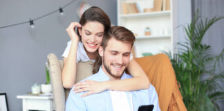 Junges Paar beim Online-Shopping zu Hause, mit dem Smartphone auf dem Sofa.