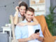 Junges Paar beim Online-Shopping zu Hause, mit dem Smartphone auf dem Sofa.
