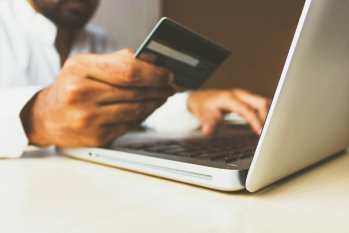 Mann vor einem Laptop mit Kreditkarte in der Hand als Symbolbild für Online Shopping.