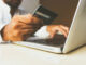 Mann vor einem Laptop mit Kreditkarte in der Hand als Symbolbild für Online Shopping.