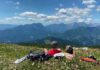 Zwei Wanderer liegen auf der Almwiese und blicken auf das Bergpanorama.