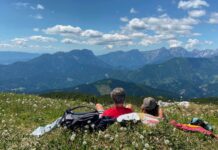 Zwei Wanderer liegen auf der Almwiese und blicken auf das Bergpanorama.