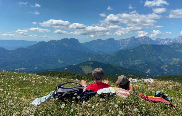 Zwei Wanderer liegen auf der Almwiese und blicken auf das Bergpanorama.