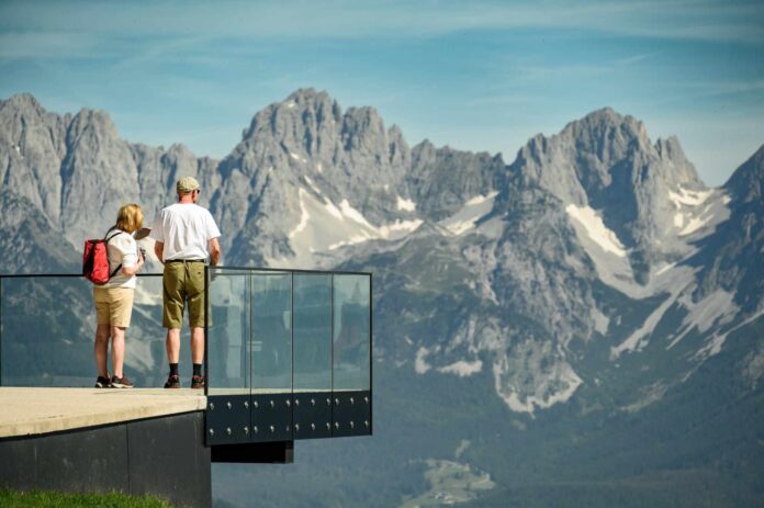 Wanderer stehen auf der Aussichtsplattform beim Starthaus vom Hahnenkamm-Rennen an der Streif in Kitzb¸hel und blicken auf die beeindruckende Berglandschaft.