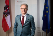 Finanzminister Markus Marterbauer stehend zwischen einer Österreich- und EU-Flagge