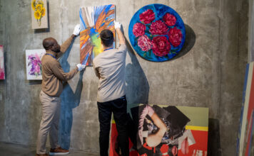 Zwei junge männliche Mitarbeiter einer Kunstgalerie hängen Gemälde an die Wand.