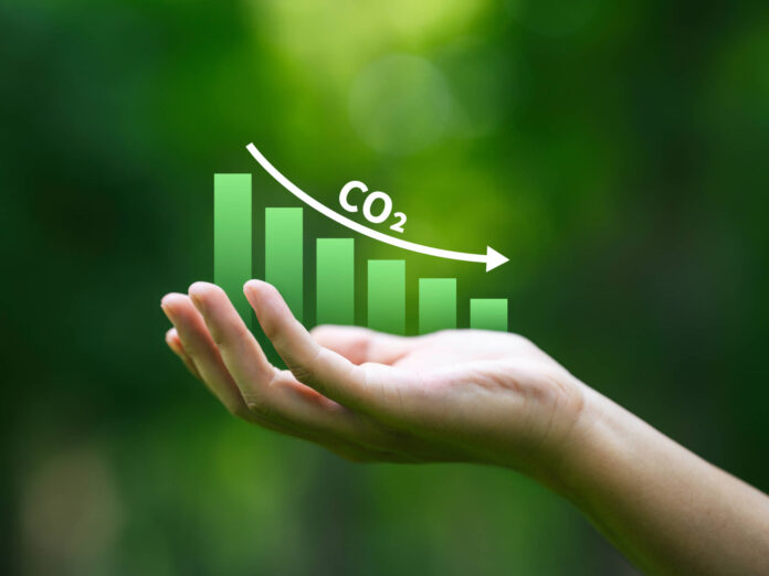 Grafik von reduzierten CO2 Emissionen in einer Hand vor grünem Hintergrund als Symbolbild für Nachhaltigkeit