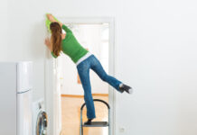 Eine Frau putzt zu Hause mit einem Bein stehend auf einer Trittleiter