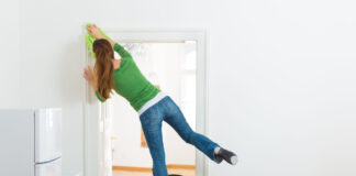 Eine Frau putzt zu Hause mit einem Bein stehend auf einer Trittleiter