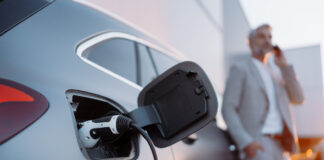 A businessman phoneing while charging car at electric vehicle charging station, closeup.