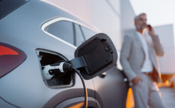 Elektromobilität zwischen Rückenwind und Steuerbremse A businessman phoneing while charging car at electric vehicle charging station, closeup.