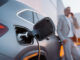 Elektromobilität zwischen Rückenwind und Steuerbremse A businessman phoneing while charging car at electric vehicle charging station, closeup.