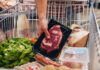 Einkauf wird preisbewusst geplant Jemand legt ein abgepacktes Stück Fleisch in einen halbvollen Einkaufswagen.