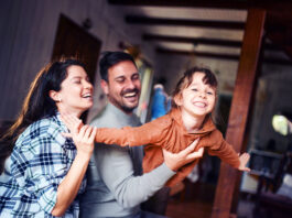 Carefree parents having fun while playing with their small daughter at home. Focus is on girl.