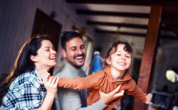 Carefree parents having fun while playing with their small daughter at home. Focus is on girl.
