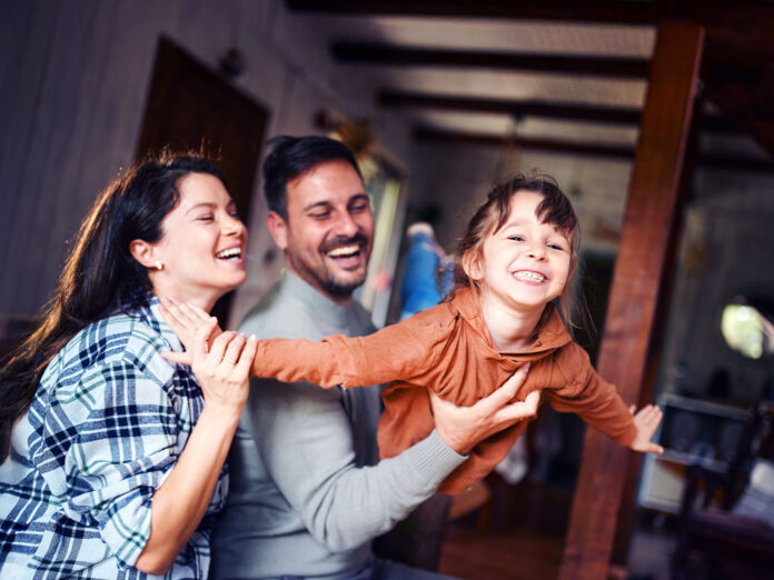 Carefree parents having fun while playing with their small daughter at home. Focus is on girl.