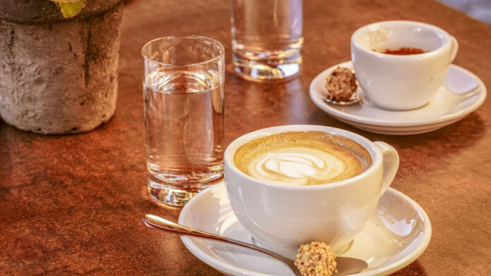 Ein Cappuccino und ein Espresso auf einem Tisch mit zwei Gläsern Wasser